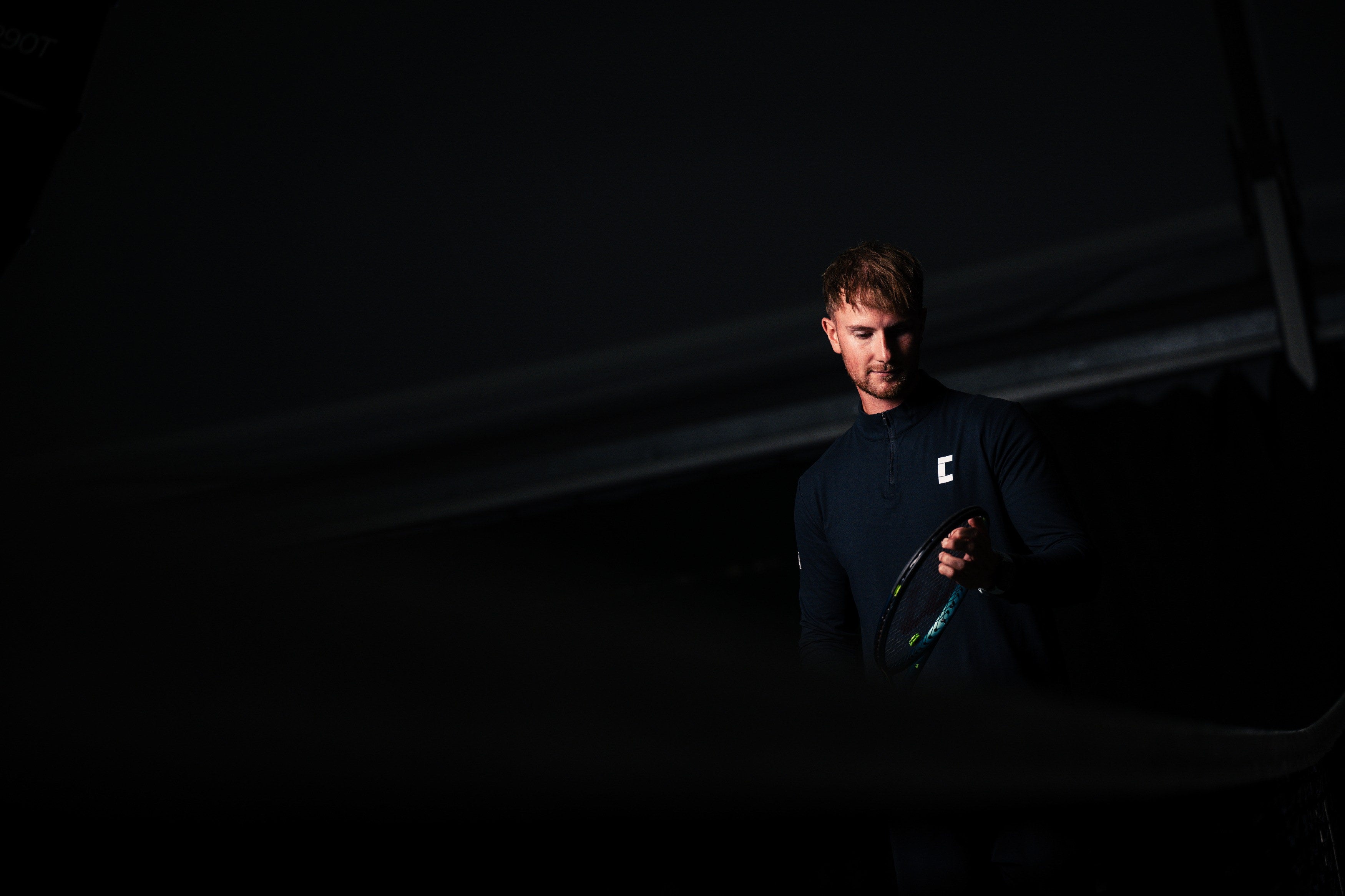 Tennis player wearing Court10 performance long sleeve with logo on a black background.