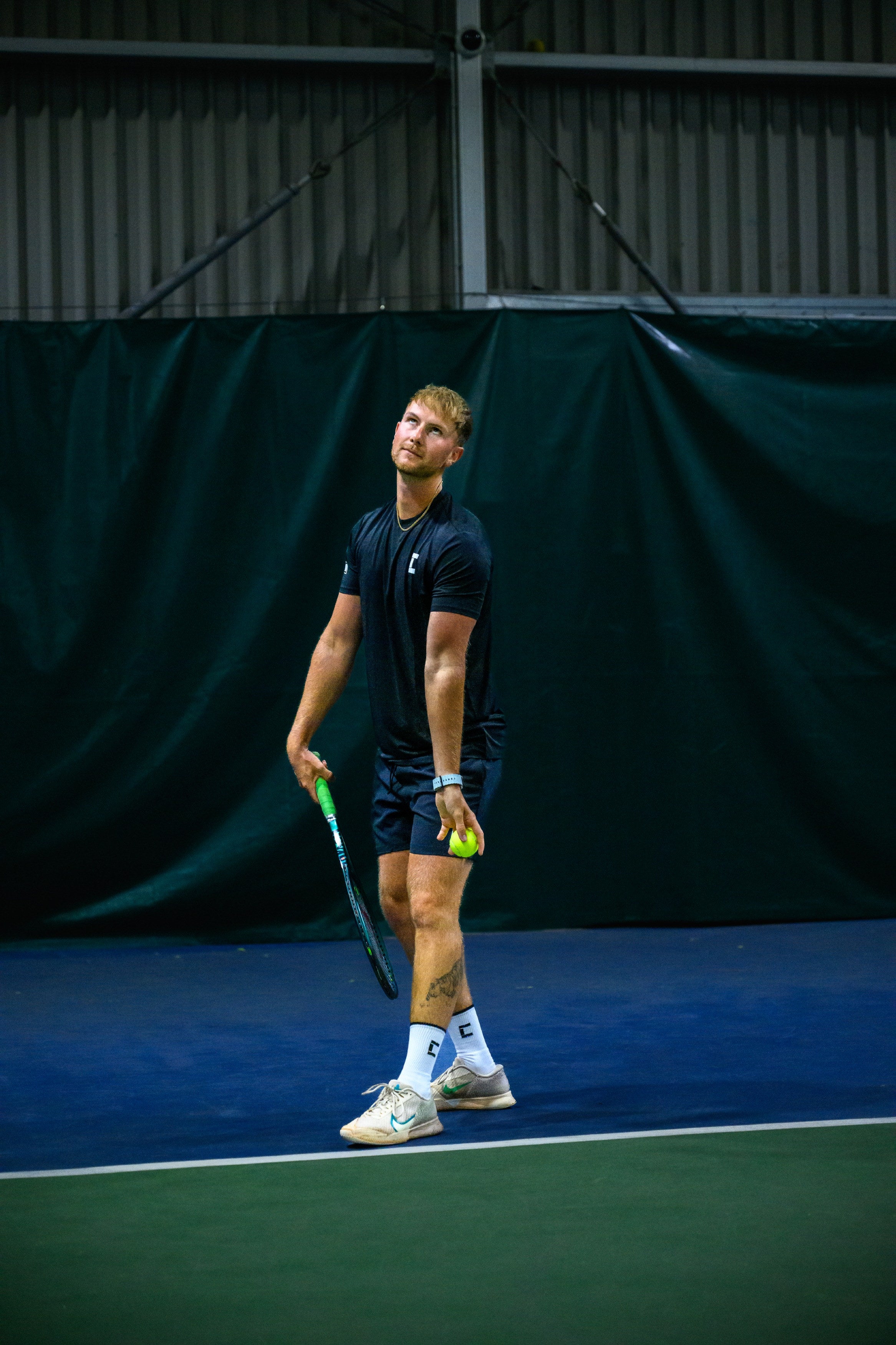 Tennis player on an indoor court about to serve.