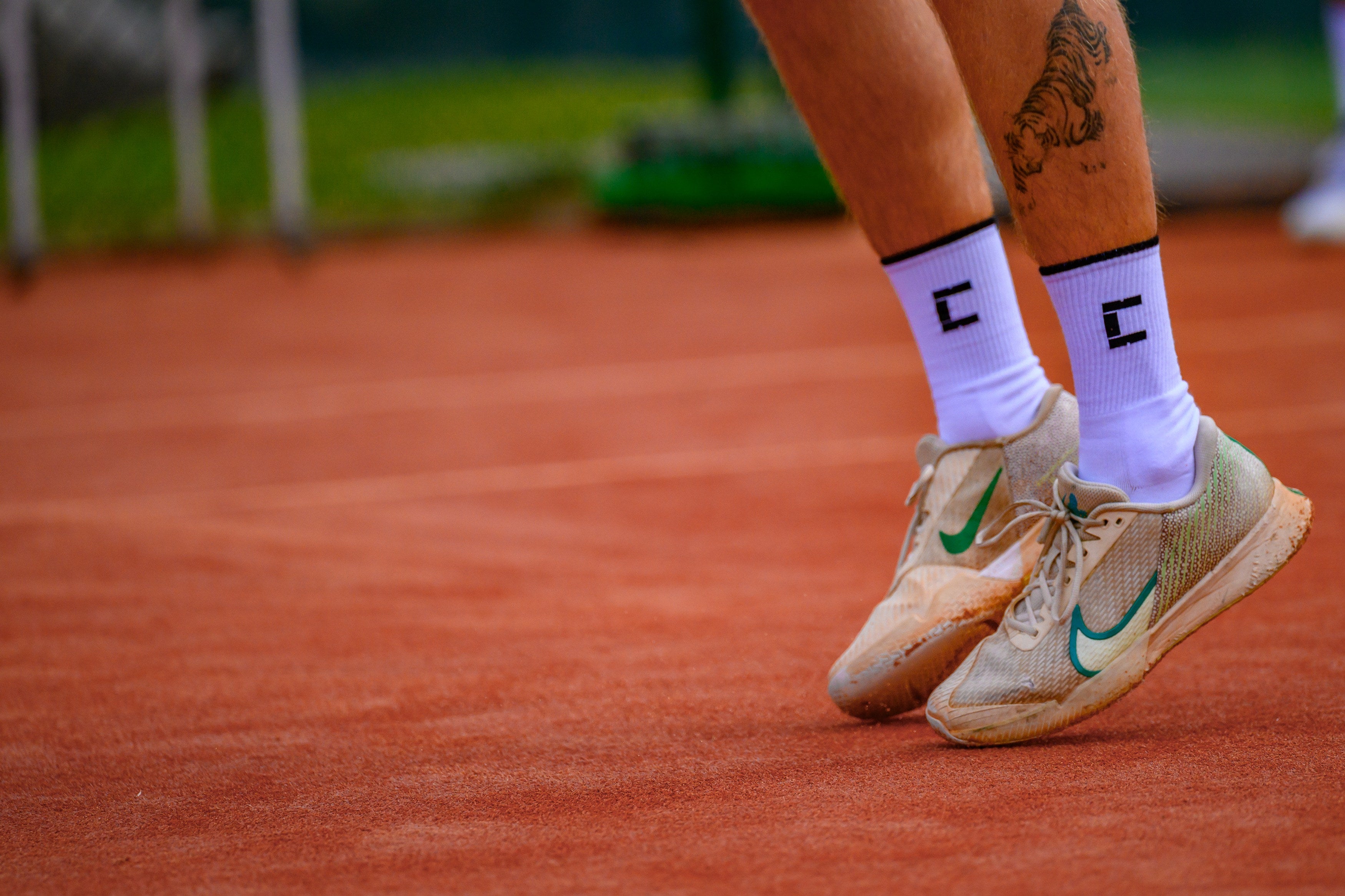 Tennis player's feet wearing beige shoes with Court10 performance socks on a clay court.