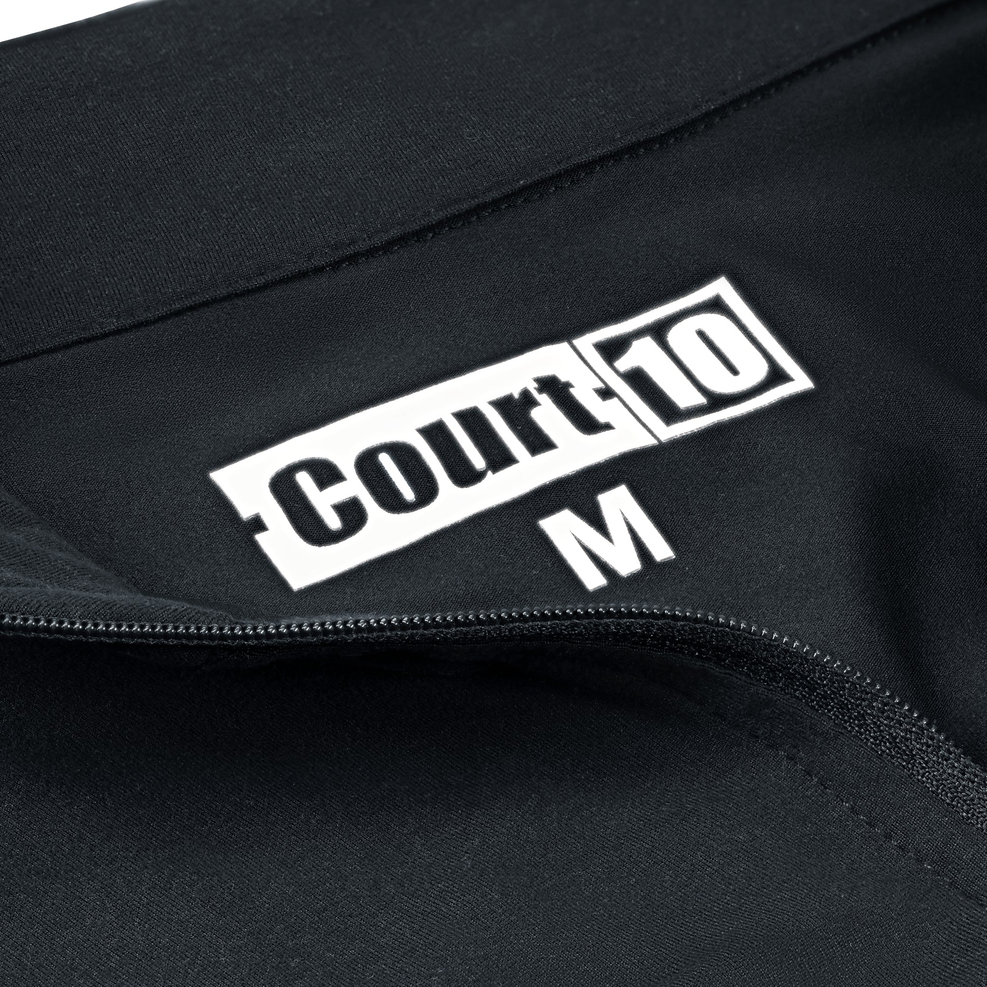 Open zip neckline detail with 'Court10' logo and size 'M' on black Performance Long Sleeve