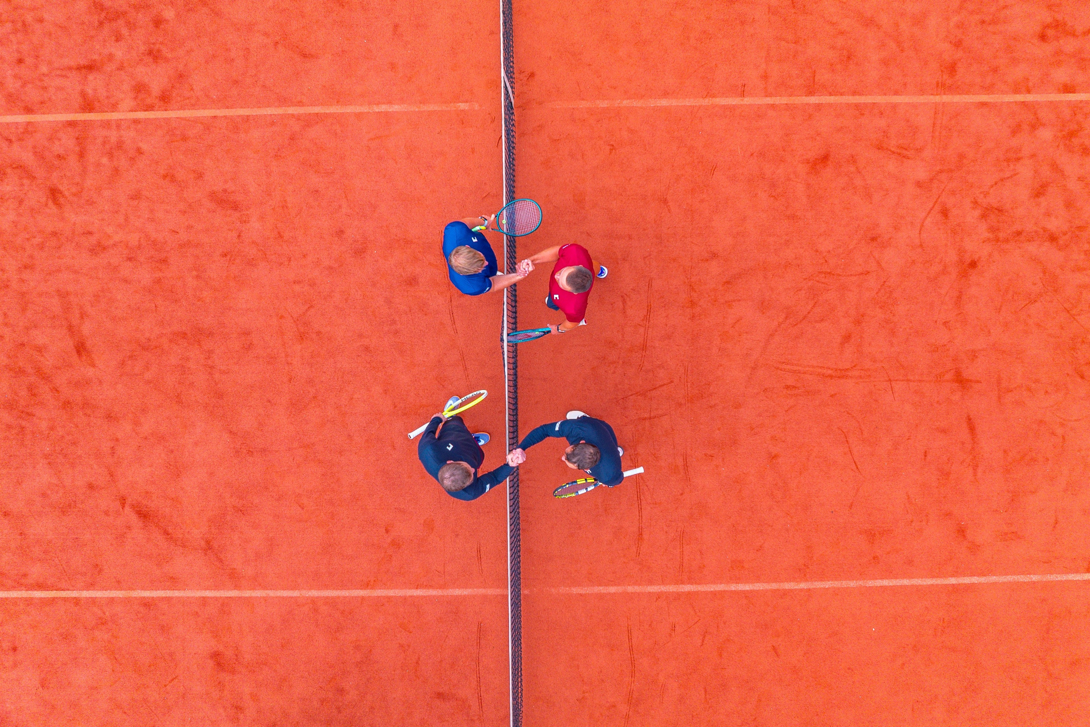 Top-down view of four people at the net on a red clay tennis court.